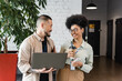 © LIGHTFIELD STUDIOS - happy african american businesswoman holding smartphone and looking at asian man with laptop