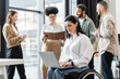 © LIGHTFIELD STUDIOS - disabled businesswoman in wheelchair using laptop near blurred multiethnic colleagues, inclusion