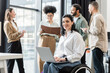© LIGHTFIELD STUDIOS - happy disabled businesswoman in wheelchair using laptop near blurred multiethnic colleagues