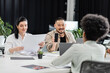 © LIGHTFIELD STUDIOS - cheerful asian man showing smartphone with blank screen to colleague in modern coworking