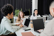 © LIGHTFIELD STUDIOS - happy woman looking at african american colleague working on laptop near asian manager in coworking