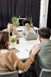 © LIGHTFIELD STUDIOS - happy multicultural business people discussing project and looking at colleague in modern coworking