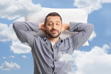 Poster - Young man in pajamas resting on a pillow in the a sky