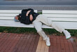 © San4ezz007 - Poor homeless man alcoholic or drug addict sleeping on a wooden bench on the street in the city.