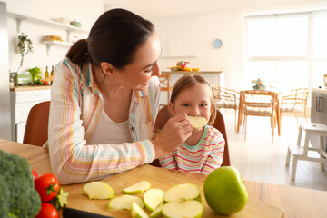 Canvas Print - Little girl with her mother eating apple in kitchen