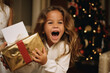 © MaryAnn - portrait of a young girl/child laughing of joy over christmas gift under tree in  festive setting wrapping gifts/presents for celebration in cinematic editorial magazine film look brown hair caucasian