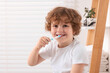 © New Africa - Cute little boy brushing his teeth with plastic toothbrush in bathroom, space for text