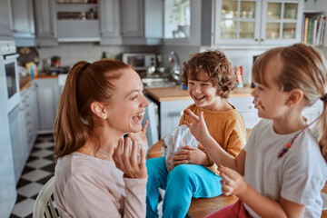 Young mother and her kids having breakfast together and being messy in the kitchen