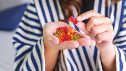 Wall Mural - Closeup image of a young woman holding and eating jelly gummy bears