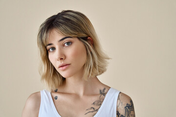 Wall Mural - Cool blonde pretty gen z girl female stylish model short blonde hair beautiful face healthy skin and tattoos looking at camera wearing white top isolated at beige background. Portrait. Copy space