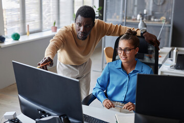 Young man pointing at monitor and discussing new computer program with his colleague in office