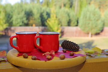 Wall Mural - A red mugs of hot tea stand on a yellow wooden tray among foliage, nuts and cone against the background of an autumn forest.