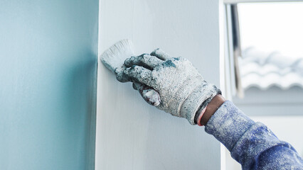 Wall Mural - A worker is painting the walls of the house with a primer using a paint roller.