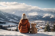 Back view child sits with toy teddy bear and looks at the winter snowy mountains.Winter family vacantion. Christmas celebration and winter holidays. Winter fun and outdoor activities with kids