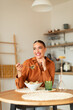 © Prostock-studio - Cheerful woman enjoying delicious caesar salad, sitting at table in kitchen, looking aside and smiling, vertical shot