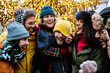 Multiethnic friends having fun together walking under Christmas tree decoration - Trendy young people celebrating x-mas holiday outside - Life style concept with guys and girls hugging on city street