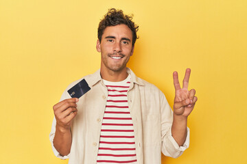 Man holding credit card on yellow showing number two with fingers.