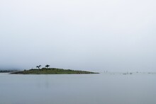 Idyllic Small Island Sits Peacefully On Top Of The Serene Lake Waters Covered By Misty Fog