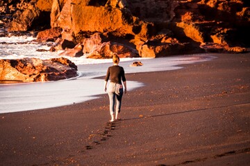 Sticker - Woman walking on the beach on a sunny day with rocks in the background