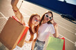 Taking a selfie. Two beautiful women in casual clothes are holding shopping bags, outdoors