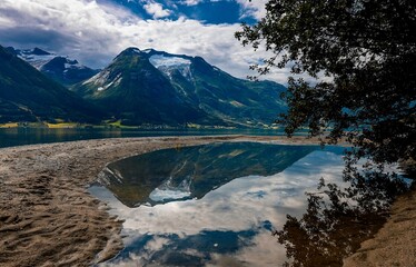 Wall Mural - Majestic mountain peaks reflected in a tranquil lake surrounded by sandy shoreline