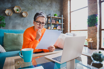 Poster - Photo of clever thoughtful mature lady dressed orange sweater reading documents working modern gadget indoors house room