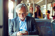 © Marko Geber - Senior Caucasian businessman using his smartphone while going to work on the bus