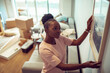 © Marko Geber - Young African American woman positioning a painting on the wall after moving in her new apartment