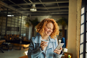 Wall Mural - Young Caucasian woman drinking coffee and using a smartphone in a startup company office