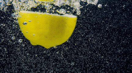 Wall Mural - Underwater of freshly squeezed sweetened lemonade which raw lemons slice falling in soda water against dark blue or black background. Close up lemonade or Highball lemon cocktail cold refreshing drink