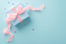 Wrapped With Care: Top View Of Pastel Blue Gift Box, Its Polka Dot Design, Pink Ribbon Bow And Tiny Hearts Exuding Joy. The Pastel Blue Background Is Ready For Your Text Or Advert
