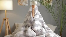 Funny Unrecognizable Female Sitting On Bed Covered With Striped Blanket Showing Empty Cup Doesn't Want Awake Without Coffee Posing In White Bedroom Interior.
