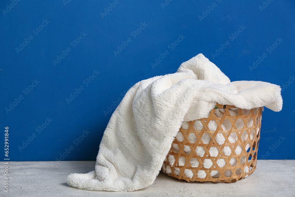 Basket with new soft blanket near blue wall