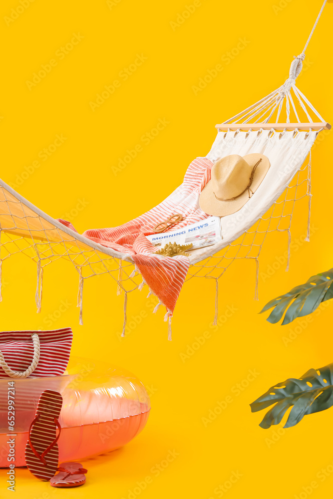 Cozy hammock with inflatable ring and different beach accessories on yellow background. Summer vacation concept
