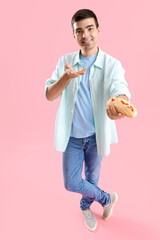 Wall Mural - Handsome young man with tasty hot dog on pink background