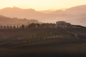 Wall Mural - Sunrise golden light over the valley of Val d'Orcia and a rustic Tuscan farmhouse in the scenic countryside landscape and rolling hills of rural Tuscany, Italy.