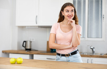 Wall Mural - Happy young woman posing near a table in a home kitchen