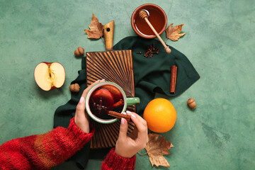 Wall Mural - Woman holding cup of hot mulled wine with apple and orange on green background