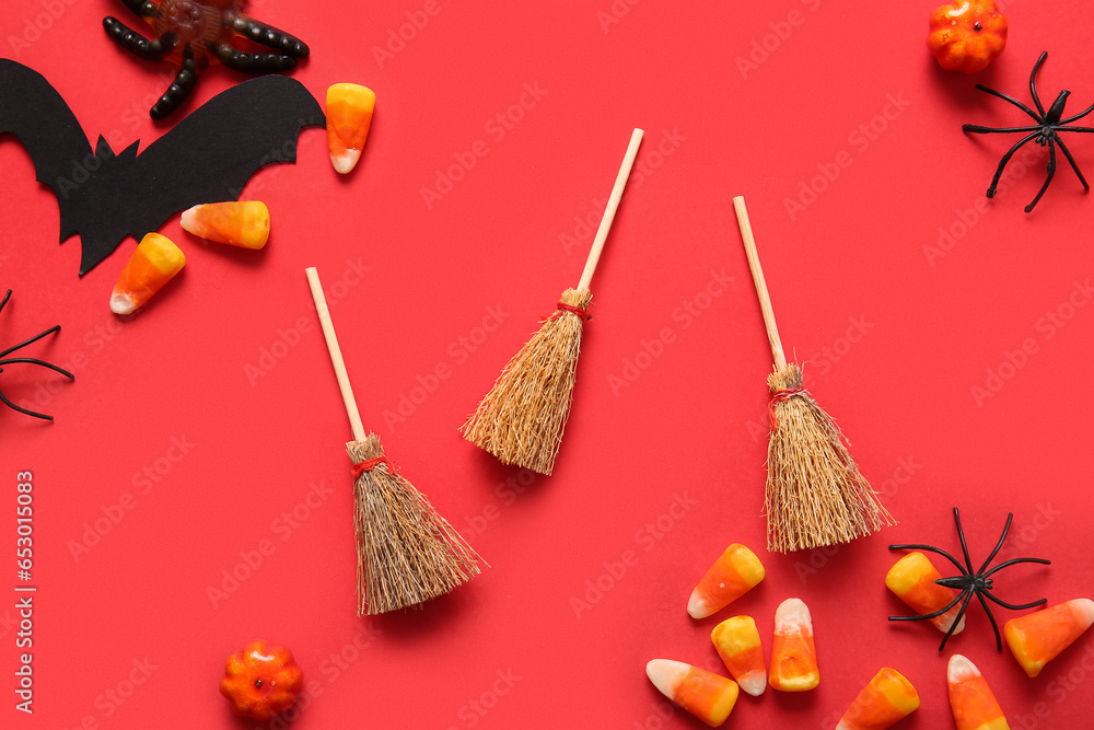 Halloween composition with brooms, candy corns and spiders on red background