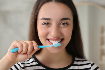 Wall Mural - Young woman brushing her teeth with plastic toothbrush indoors, closeup