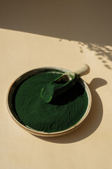 Wall Mural - Organic blue-green algae spirulina powder food in plate with wooden spoon. Copy space for your text Health benefits of spirulina chlorella. Vitamins and minerals to diet. Detox dietary supplement