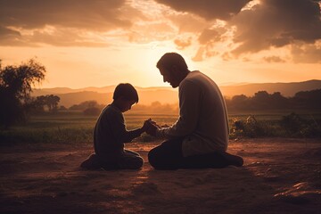 Father and son together praying on knees in beautiful sunset.