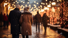 Back View Of Couple Walking On Snowy Street With Christmas Lights On Background