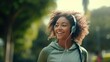 Smiling black woman in sports clothes running in a green park enjoying listening to music with wireless headphones close-up