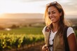 Portrait of happy young woman with backpack in vineyard at sunset