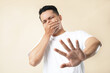 © Illhamt - A photo of an Asian young man holding his nose against a bad smell, wearing a white t-shirt, and isolated on a cream background.