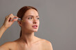© New Africa - Beautiful young woman applying cosmetic serum onto her face on grey background, space for text