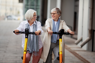 portrait happy smiling senior women with gray hair enjoying ride together on electric scooters outdo