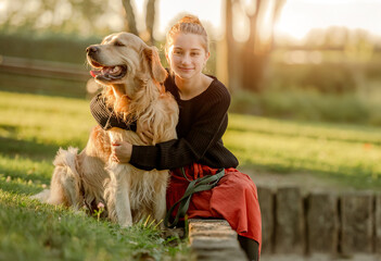 Wall Mural - Pretty girl with golden retriever dog sitting at nature and smiling. Beautiful female model teenager hugging purebred pet doggy at autumn park