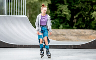 Sticker - Beautiful girl roller skater riding in city park with ramp. Pretty female teenager rollerskating in casual clothes